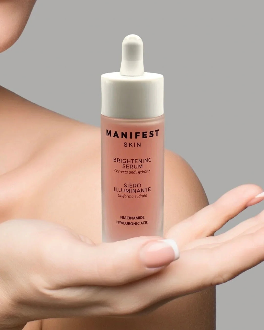 Siero illuminante Manifest Skin con niacinamide e acido ialuronico tenuto in mano su sfondo neutro