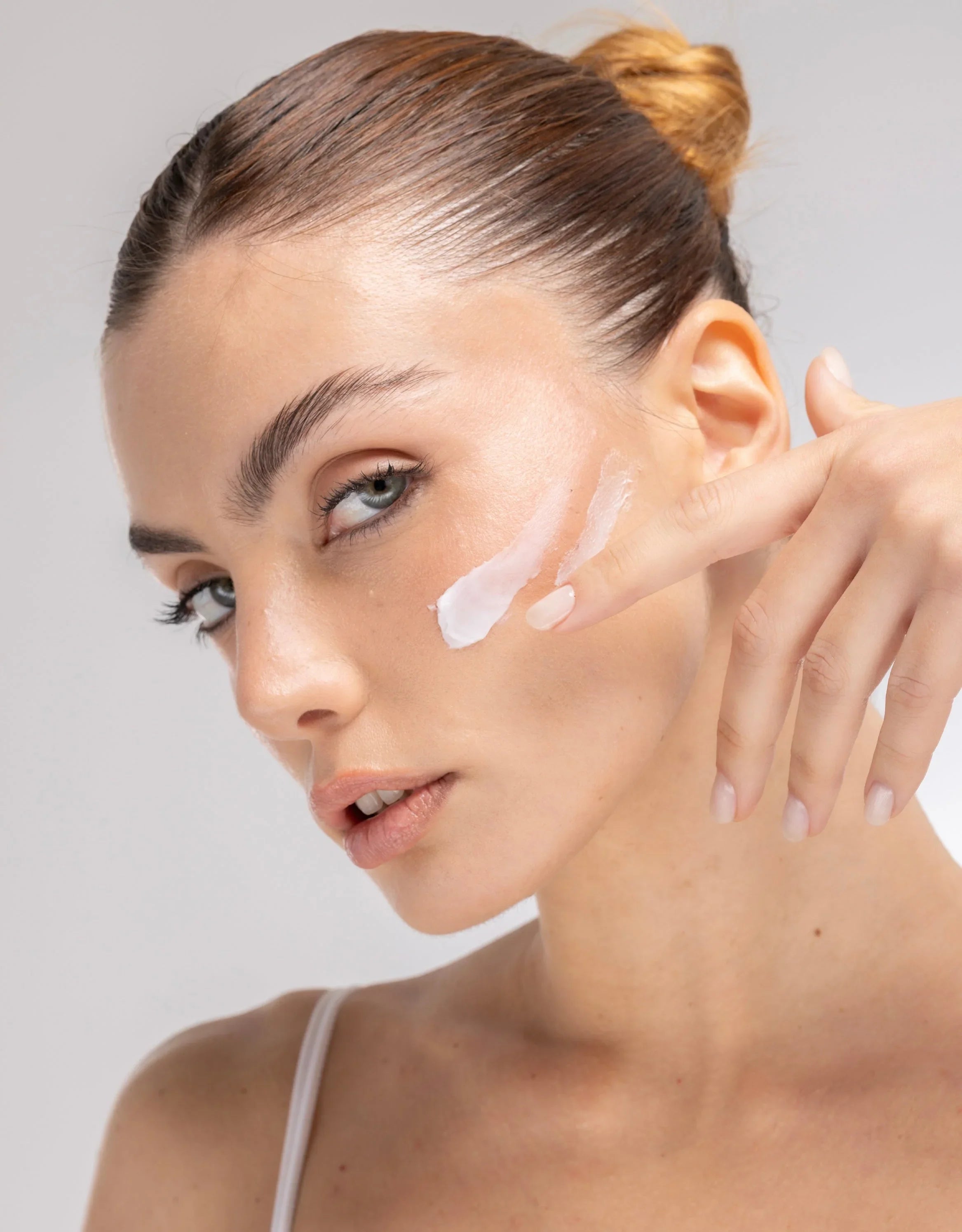 Donna applica crema idratante viso per skincare Glow su guancia, beauty Buzz Skin